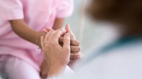 A stock image of a patient's hands holding a carer's hands. Just the hands are in shot.