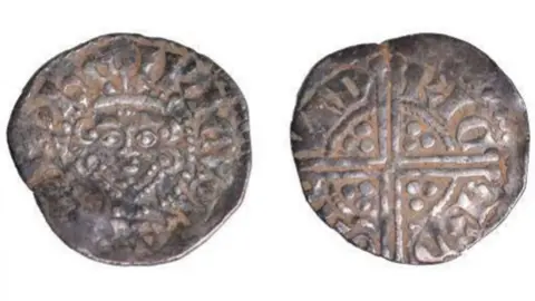 Record of Treasure Inquest A silver Medieval coin photoaged from the front and back. The coin is shiny with a Celtic cross engraved on one side and a monarch's face on the other.