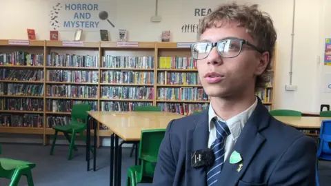A teenager wearing glasses and a traditional blue school uniform with a white shirt and blue striped tie