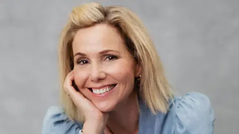 Courtesy of Stratford Literary Festival A close-up photo of a woman in front of a plain grey background. She has blonde hair and is wearing a pale blue shirt.