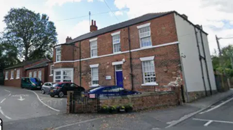 A screenshot from Google streetview of a brick school building with cars parked at the front. 