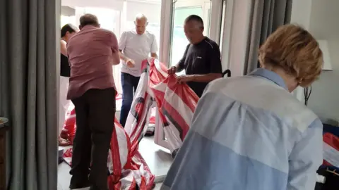 This is Wearside People are in a house folding up a large red and white flag.