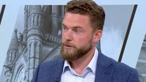 Phil Eckersley, wearing a light blue shirt under a dark blue jacket