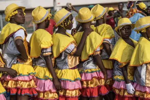 Marco Longari / AFP Girls wearing matching yellow and pink ra-ra skirts stand in a line.