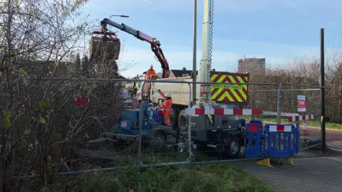 Metal fencing with diggers and workers in orange high vis working to repair a burst water main.