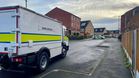 A bomb disposal lorry with a police car in the background