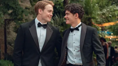 Production still from Heartstopper Forever showing Kit Connor and Joe Locke smiling at each other in tuxedos