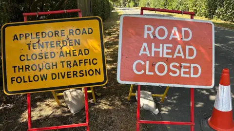 Oliver Whitfield-Miocic/BBC One road sign that reads "road ahead closed" and another reads Appledore Road Tenterden closed ahead through traffic follow diversion.