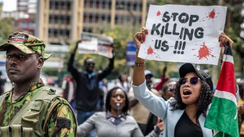 A protester holds a sign saying 'stop killing us'.