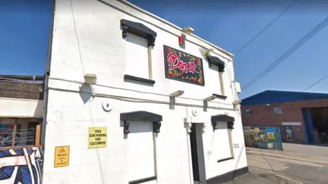 The entrance to Dare To club in St Philips. The brick of the building is painted white and the sign is hand painted in black and red.