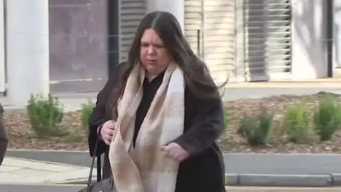 Amy Rees wearing a beige scarf and wearing a black jacket arrives in court.