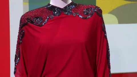 A red jumpsuit with beads in a geometric pattern on its shoulders and sleeves.