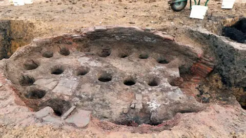 The remains of a brick pottery kiln can be partially seen in the ground where excavators have worked.