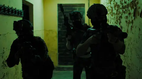 Sunray: Fallen Soldier Three men in military gear and guns walk down an unlit corridor as part of a film still from Sunray. 