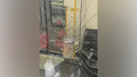 A train window with a smashed hole in the centre of it, with glass cracks coming out of it.