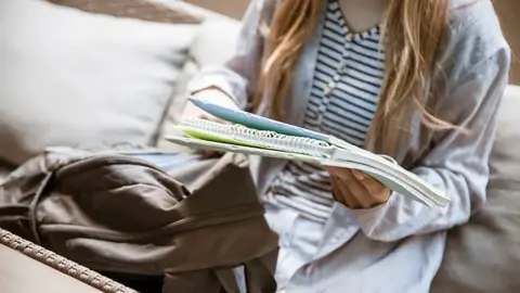 A young person with long hair holds a notepad. Their face is out of vision.