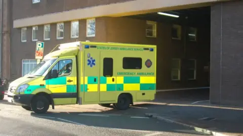 BBC A States of Jersey Ambulance Service emergency ambulance driving out of the hospital building entrance in Jersey.