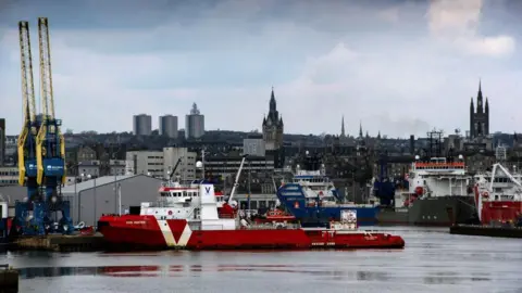 Image of Aberdeen harbour, offshore industry vessels in the water, with the city skyline in the background.