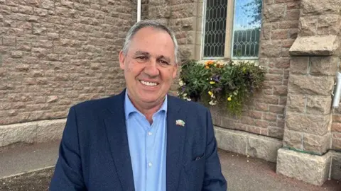 Man in blue suit in front of Parish Hall