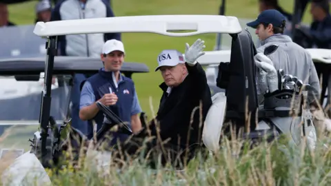 PA Media Donald Trump waves to onlookers from his golf buggy