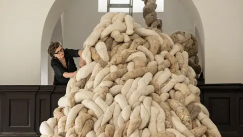 A woman arranges a huge woollen sculpture in an old building