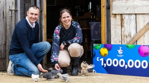 PA Graeme and Katherine White with bantam hens and a £1m Lottery sign in front of a barnd 