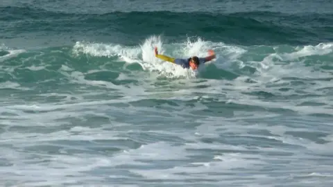 Danny Teare wearing a colourful wetsuit surfing a wave with both of his arms stretched out wide propelling him through the wave.
