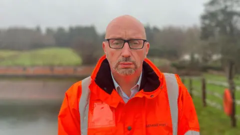 A bald man in glasses. He is wearing an orange jacket. 