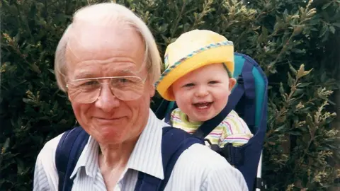 Supplied Philip Hendy smiling and carrying a baby on his back.