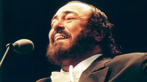 Getty Images Pavarotti, dressed in distinctive opera jacket and white bow tie, singing into a microphone