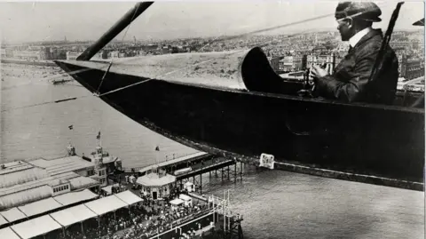 Black and white image of a seaplane flying over Brighton pier circa early 20th Century
