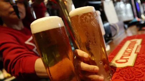A bartender puts down two pints of beer on the table. 