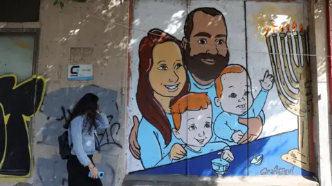 EPA A woman walks past a street artwork depicting the Bibas family on a wall in Tel Aviv