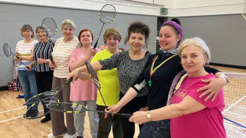 Shariqua Ahmed/BBC A group of women standing in a row holding badminton rackets.