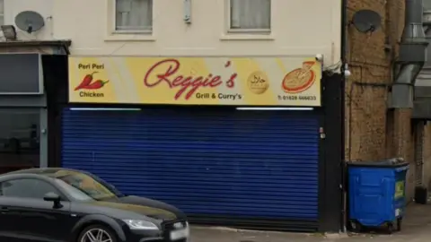 Google A picture of the scene outside Reggie's, which has blue shutters and a yellow sign.  