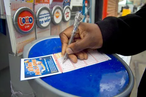 Photo of a hand filling out a EuroMillions ticket at a booth in a corner shop