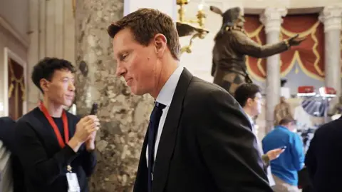 Getty Images David Ellison in a dark suit and tie in profile walking through Congress. Behind him there is a person wearing a lanyard and clasping his hands together