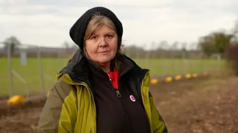 Martin Giles/BBC Alison Downes standing next to a construction site for the new access road to Sizewell C