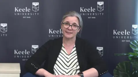 BBC / Harry Craig Dr Helen Wells is sat on a chair in front of a dark grey wall covered in the Keele University logo. She is looking directly at the camera face-on and talking.