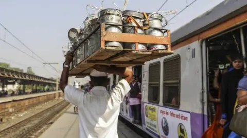 Dabbawala Dasharath Kedari carries a crate of tiffin boxes while walking past a train at the Santacruz railway station in Mumbai, India