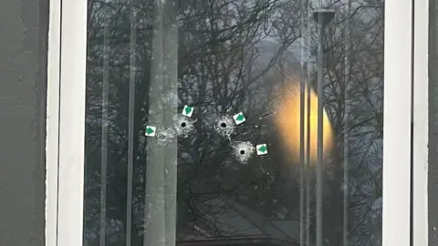 BBC Four small bullet holes are left on a large pane of glass. There are small arrow stickers placed at each hole.