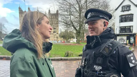 A police officer and a woman wearing a green rain coat standing in front of Exeter Cathedral