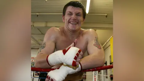 PA Ricky Hatton smiling and sweaty stood on the edges of a boxing ring making a thumbs-up sign.