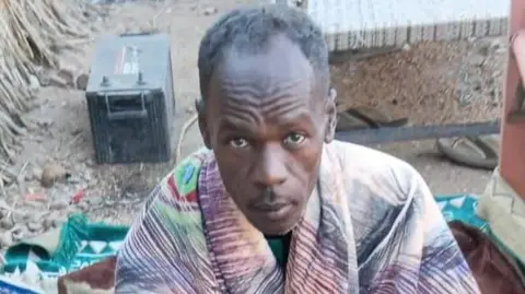 Mohamed Suleiman looks up at the camera, he has a blanket around his shoulders.