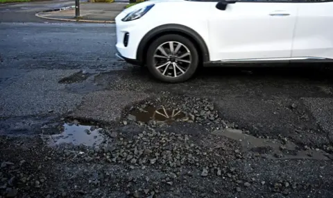 Getty Images Sebuah mobil putih melaju melewati beberapa lubang di jalan di Inggris