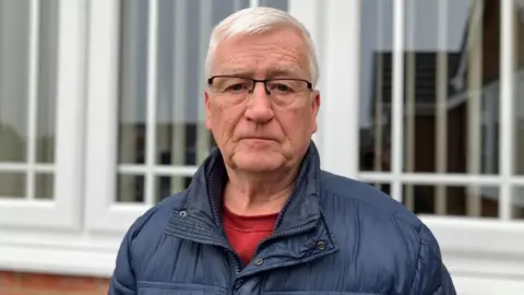 Man in blue jacket outside his home