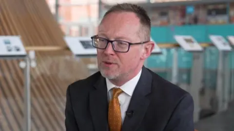 BBC Russell George sat on a chair in front of the funnel at the centre of the Senedd building in Cardiff Bay.