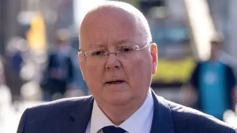 Peter Murrell, who is bald with glasses, wearing a business suit while outside 