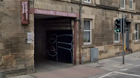 Google A garage entrance in a sandstone tenement block bears a small sign marking the offices of Capital Cars. 