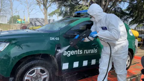 An official wearing white protective clothing as he sprays his car with disinfectant after patrolling an area that has seen an outbreak of the swine fever